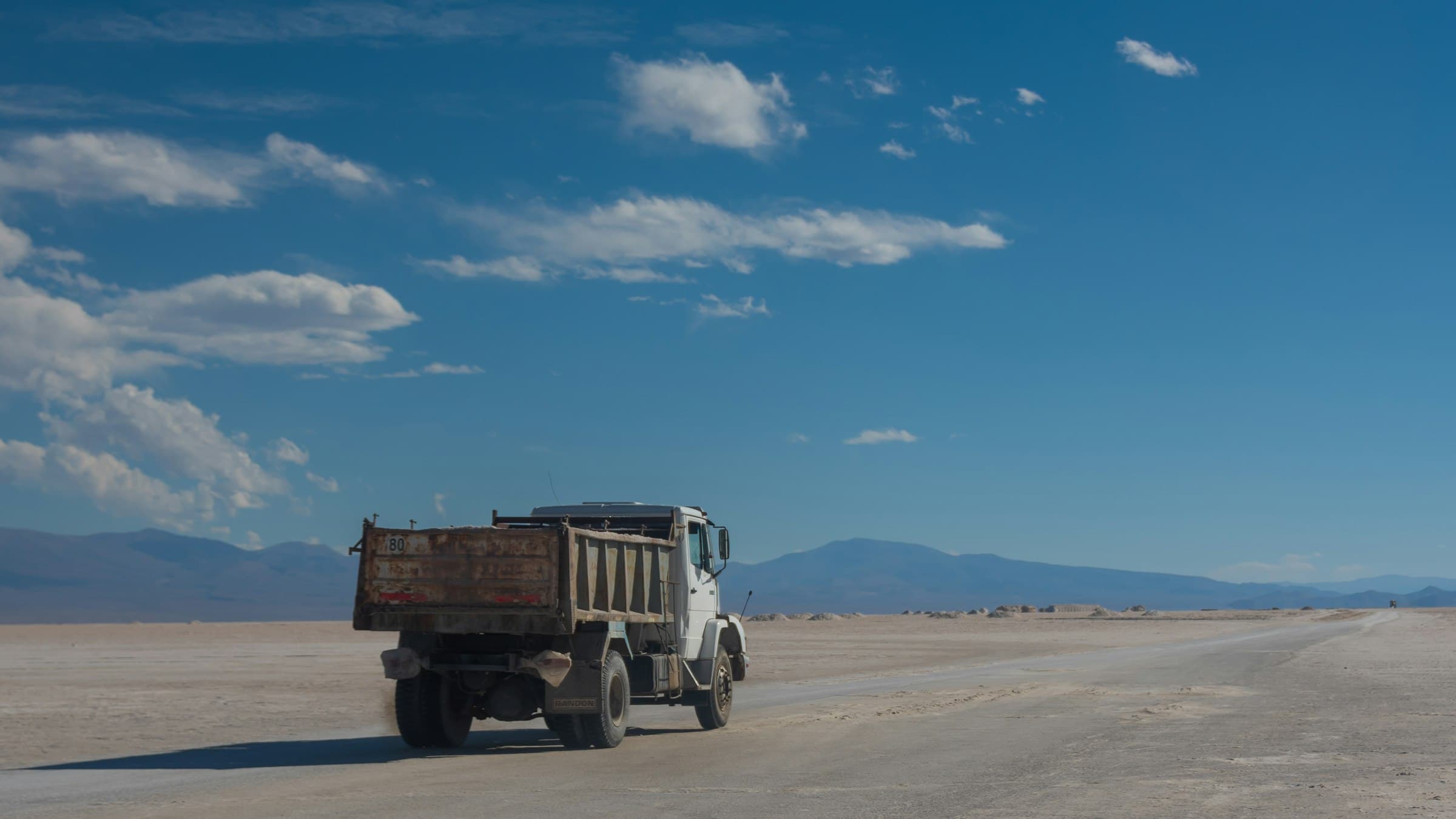 Truck driving across a wide open salt flat under a blue sky